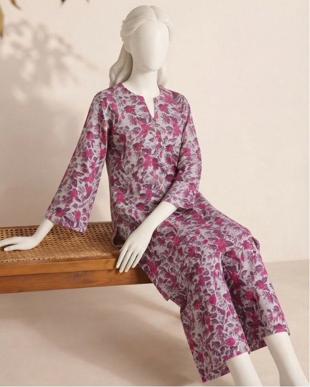 A mannequin wearing a Dhanak unstitched 2-piece kurta set with a pink and purple floral pattern on a light gray base, seated on a wooden bench against a beige wall.