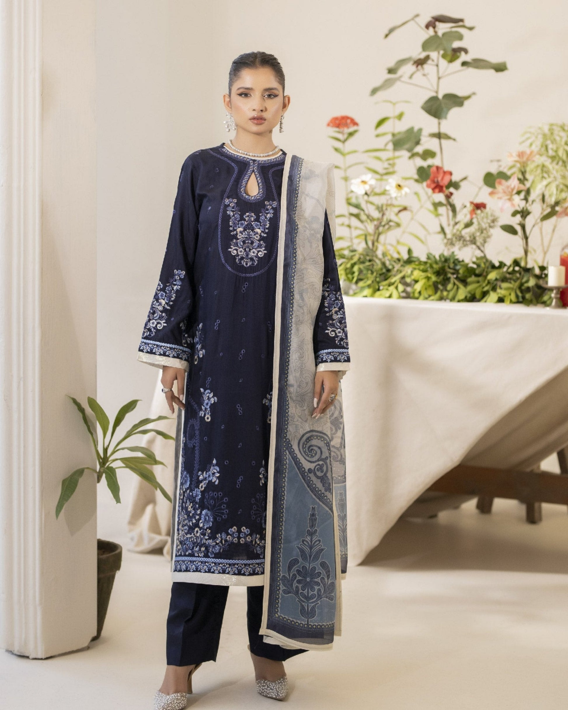 A woman wearing a navy blue embroidered shirt with long sleeves, paired with a matching dupatta and trousers. The clothing features floral and geometric patterns.
