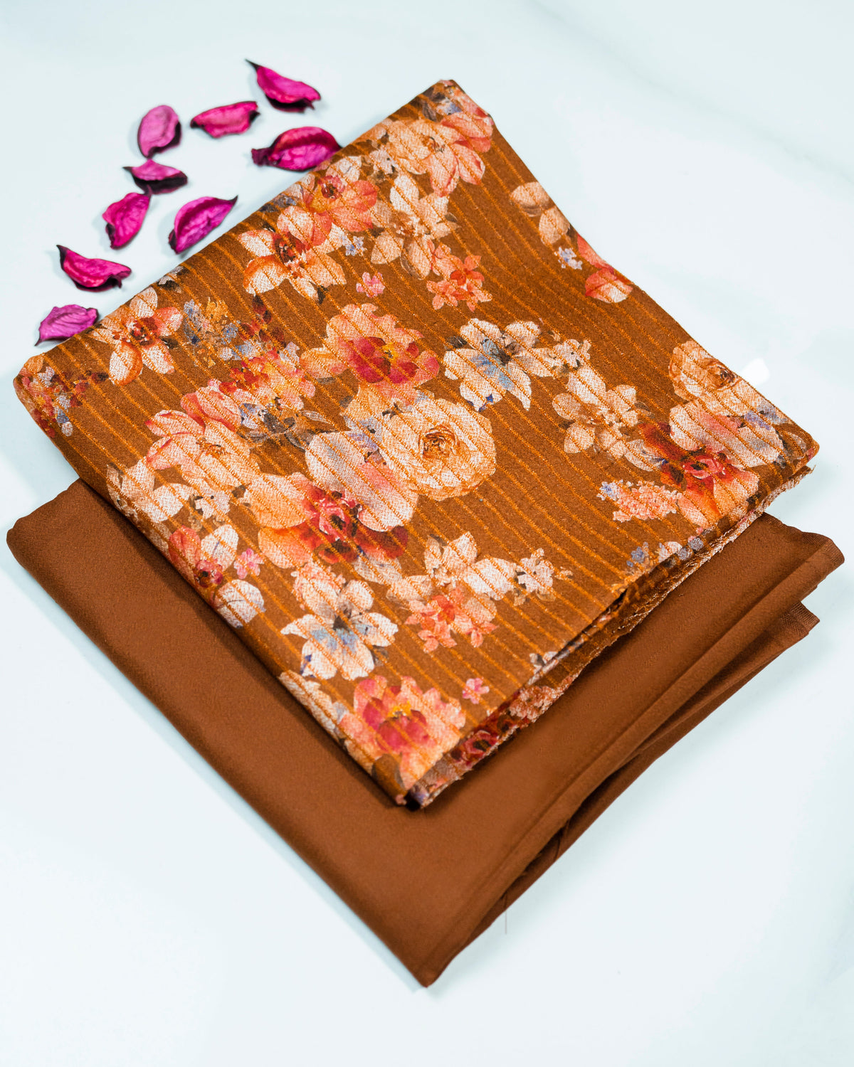 Floral fabric on top of plain brown fabric with pink petals on a white background