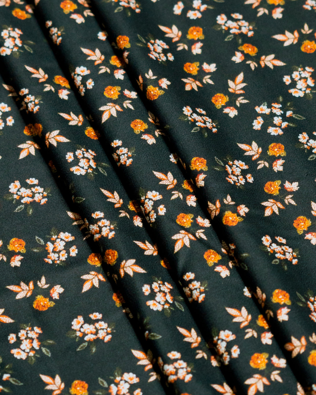 A close-up of a dark pine green fabric with a small orange and cream floral print, styled with wooden pepper mills and a yellow object in the foreground.
