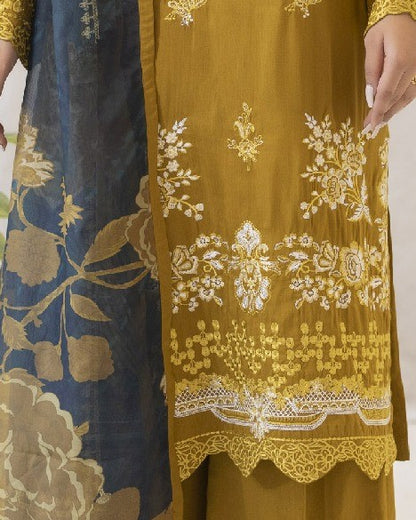 Close-up of a mustard yellow fabric with intricate white embroidery on a plain background