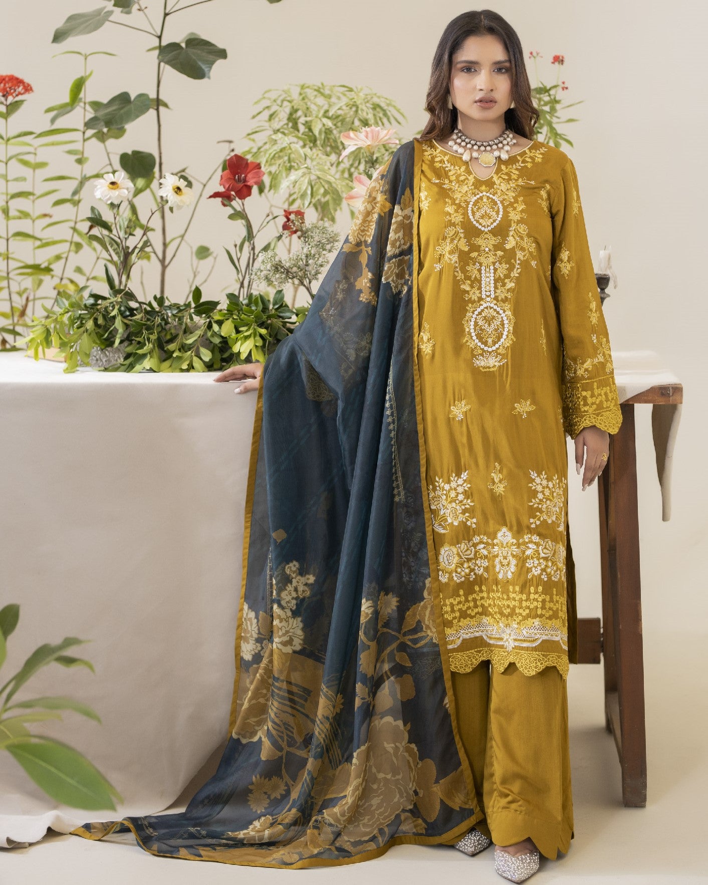 Woman in mustard yellow embroidered outfit with blue dupatta against a white background