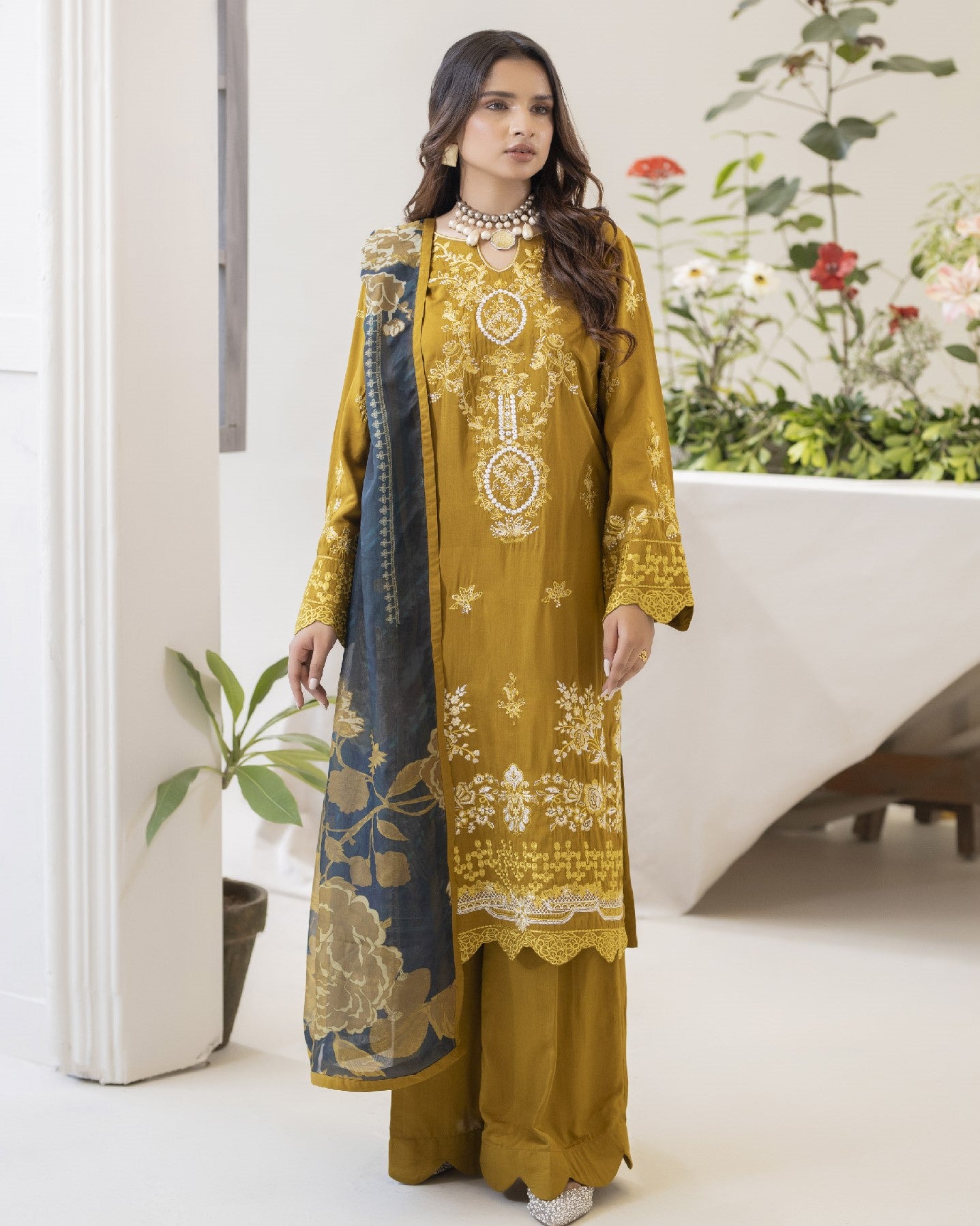 Woman wearing a mustard yellow embroidered outfit with a matching dupatta in a minimal indoor setting.