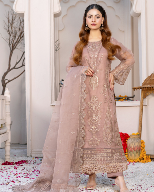 A woman wearing a traditional embroidered dress in a beige color with floral patterns, paired with trousers, standing in a decorative setting.