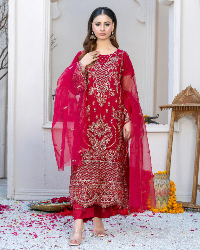 A woman wearing a traditional red and embroidered dress with a dupatta, standing in a beautifully decorated room with a white throne in the background.
