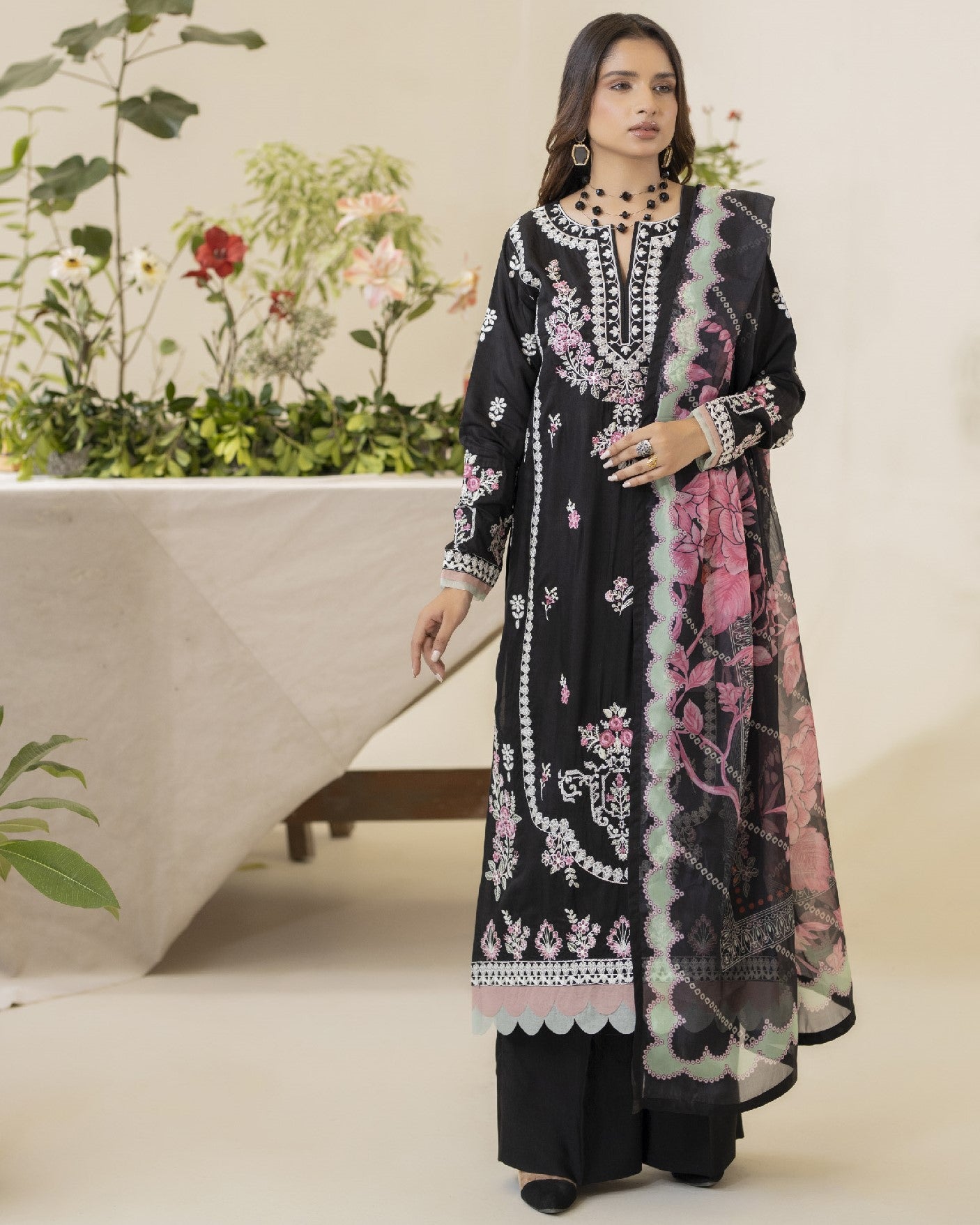 Woman wearing a black embroidered dress with pink floral patterns in a minimalistic setting.